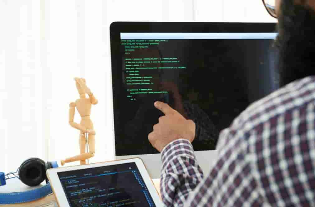 man in shirt pointing on the computer screen with green coding on black screen on it